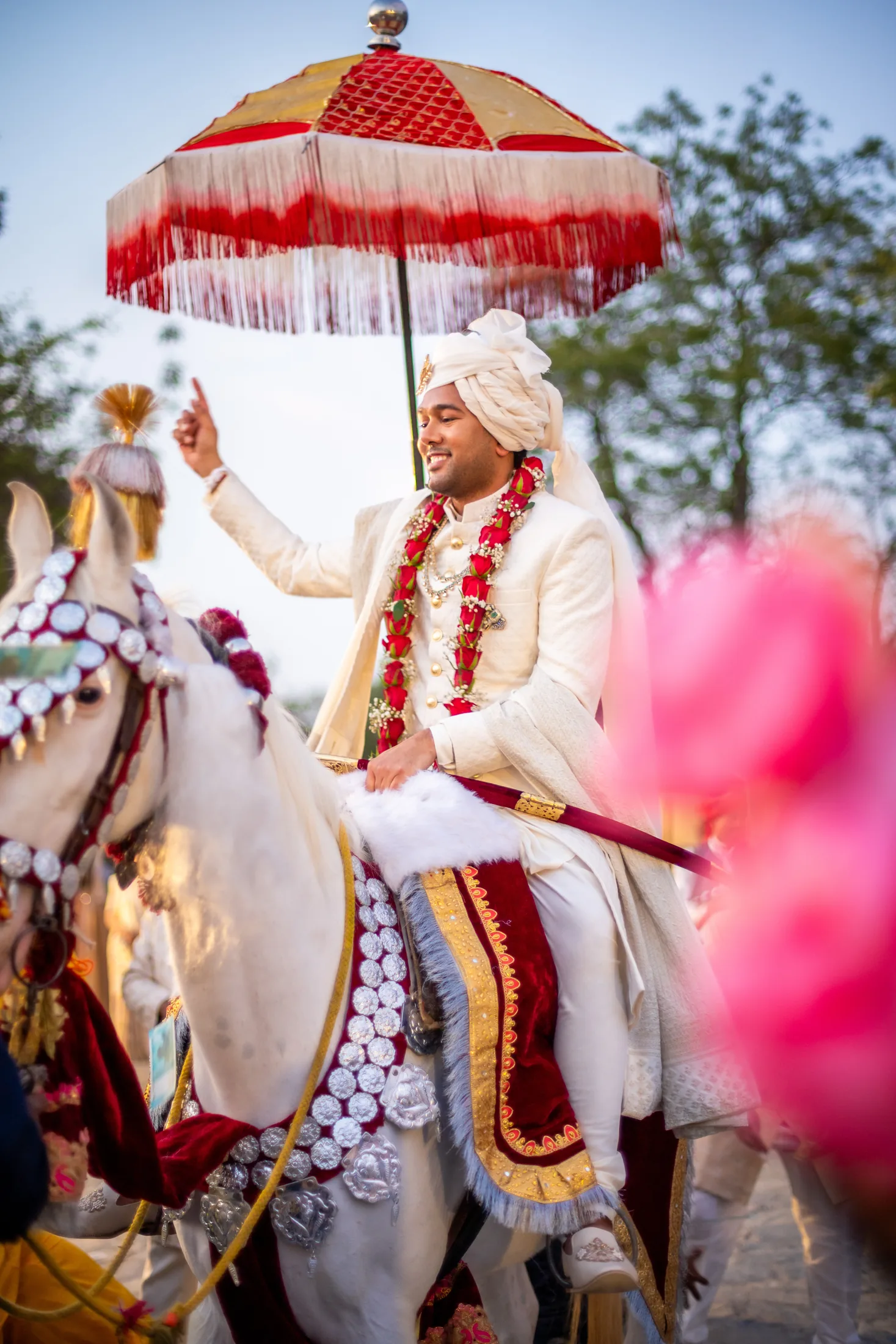 Jay arrives on a white horse beneath a red and gold wedding umbrella