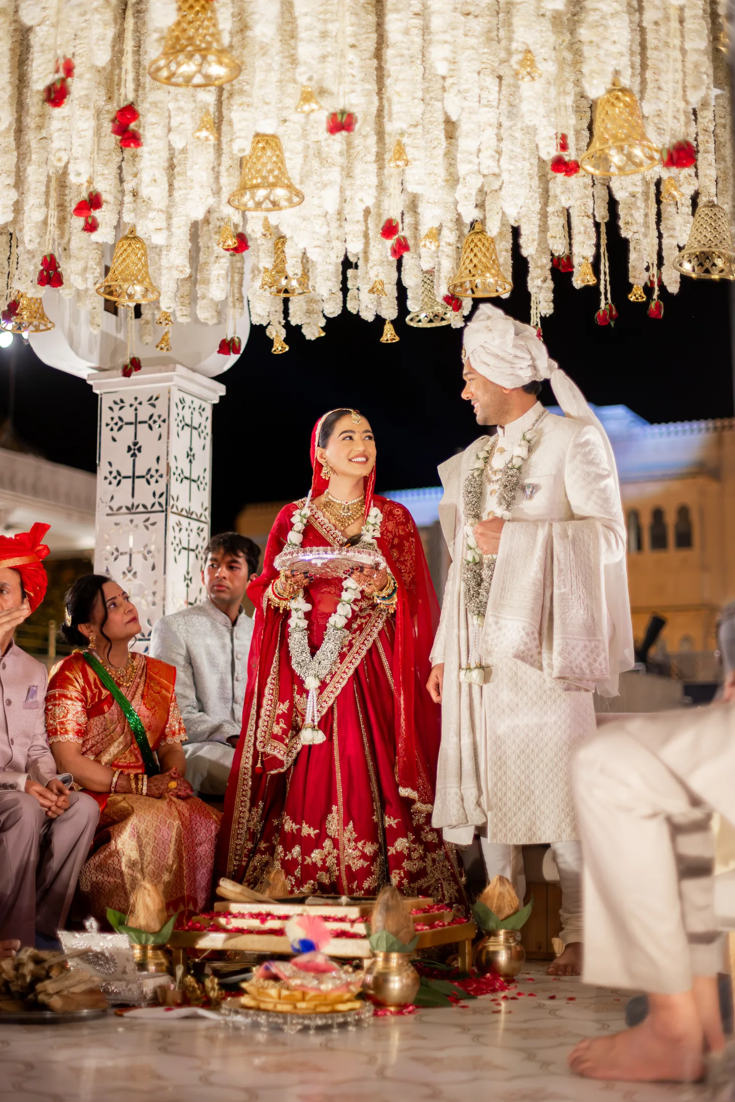Jay and Serene stand together under white flowers and gold ceremony bells